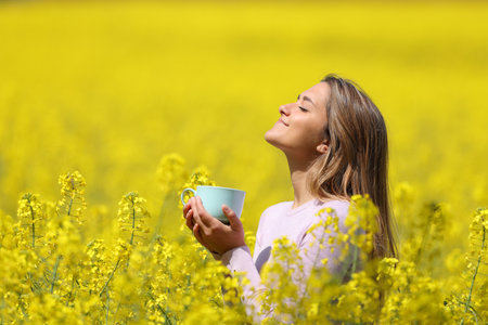 Profile of a happy woman relaxing breathing deeply fresh air and holding a coffee cup in a yellow fieldの写真素材