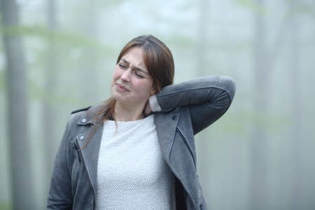 Woman suffering neck ache complaining alone in a foggy forestの写真素材