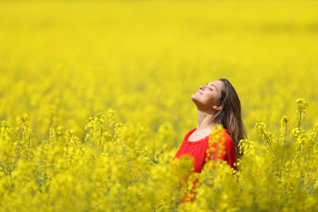 Relaxed woman in red breathing fresh air in a yellow field in spring seasonの写真素材