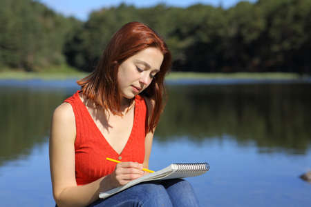 Concentrated woman drawing on notebook sitting in a lake in the mountainの写真素材
