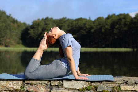Profile of a woman practicing yoga pose in a lake in the mountain a sunny day