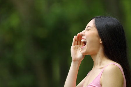 Profile of an asian woman shouting with hand on mouth in a parkの写真素材