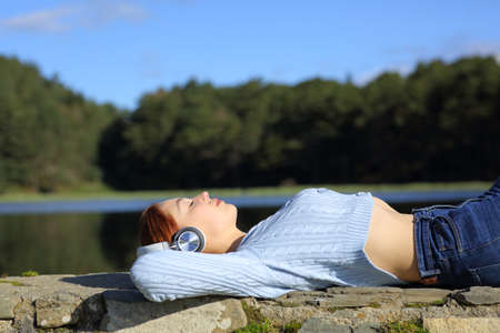 Side view portrait of a woman relaxing listening to music with wireless headphones in a lake in the mountainの写真素材