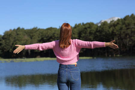 Back view portrait of a casual woman stretching arms celebrating vacation in a lakeの写真素材
