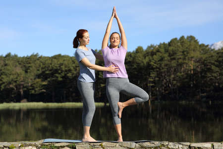 Front view portrait of a yogi teaching yoga to a woman in a lakeの写真素材
