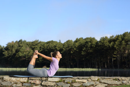 Profile of a woman doing yoga pose in the mountain beside a lakeの写真素材