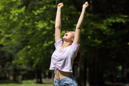 Excited casual woman raising arms in a park or forest a sunny day