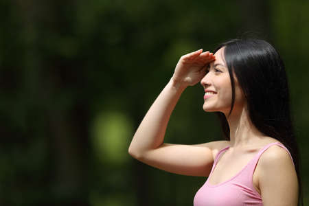 Side view portrait of a happy asian woman watching protecting from sun in a parkの写真素材