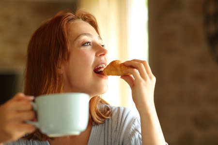 Happy woman eating and drinking for breakfast in the living room at homeの写真素材