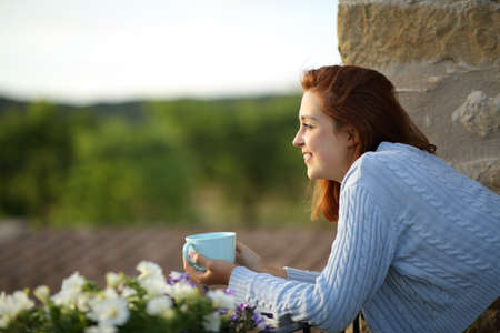 Side view portrait of a happy woman contemplating from balcony with coffee cupの写真素材