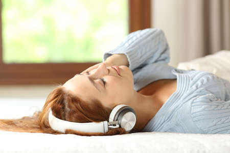 Woman relaxing on bed listening to music with wireless headphones at homeの写真素材