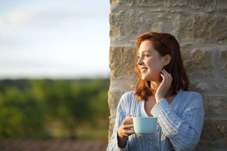 Happy woman at sunset drinking coffee contemplating views from a balconyの写真素材