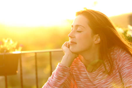 Relaxed woman feeling with closed eyes sitting in a balcony at sunsetの写真素材