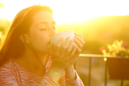 Woman relaxing drinking coffee in a balcony at sunsetの写真素材