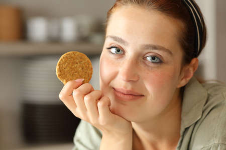 Satisfied woman posing holding a cookie in the kitchenの写真素材