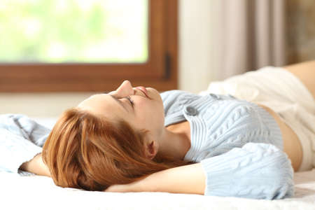 Satisfied woman relaxing resting on the bed at homeの写真素材