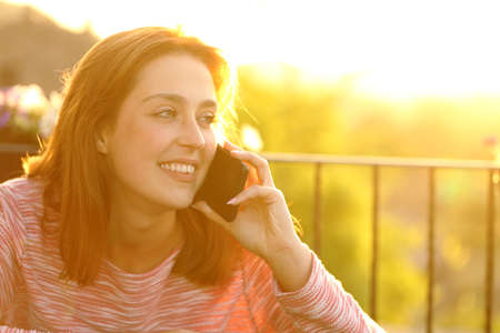 Happy woman talking on mobile phone in a balcony at sunsetの写真素材