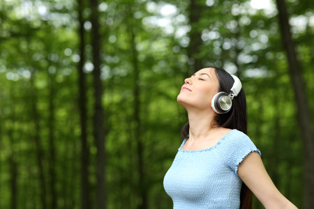 Asian woman listening to music wearing headphones breathing fresh air in a forestの写真素材