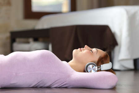 Side view portrait of a woman lying on the floor listening to music with headphones in the bedroomの写真素材