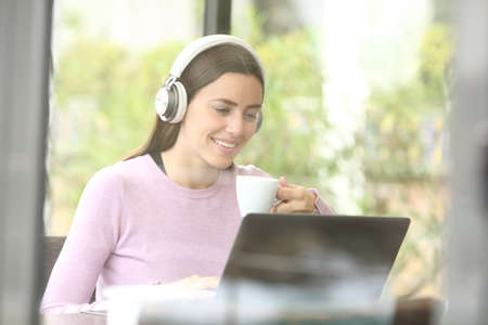 Happy female using laptop and wireless headphones in a coffee shop