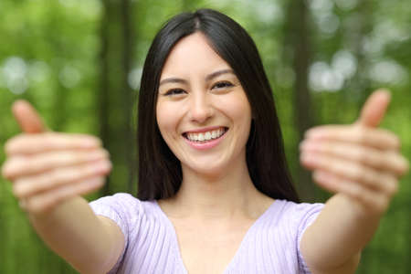 Front view portrait of a happy asian woman beckoning come here inviting you in a parkの写真素材