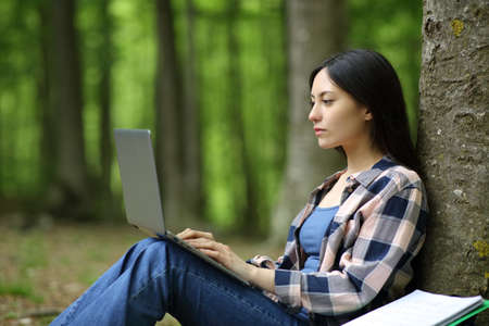 Concentrated asian student e-learning with laptop in a forestの写真素材
