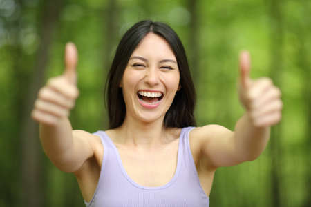 Front view portrait of an asian happy woman with thumbs up in a green forestの写真素材