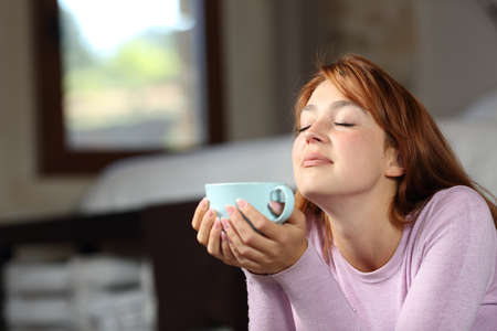 Woman relaxing breathing and holding coffee cup lying on the floor in the bedroomの写真素材