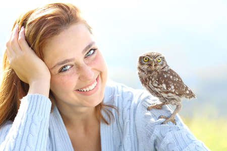 Beautiful woman with blue eyes posing with an owlet looking at cameraの写真素材