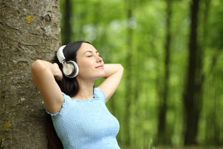 Asian woman resting listening to music wearing wireless headphones relaxing in a forestの写真素材