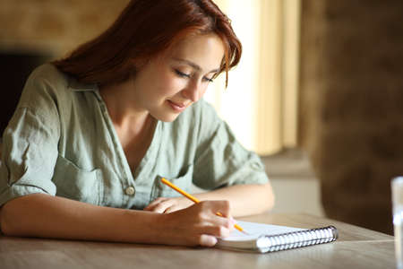 Woman drawing or taking notes on paper notebook on a table at homeの写真素材