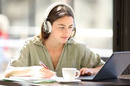 Concentrated student e-learning with a laptop and headphones in a coffee shopの写真素材