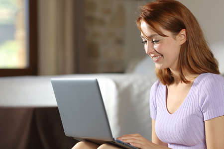 Happy woman using laptop sitting on the floor in the bedroom at homeの写真素材