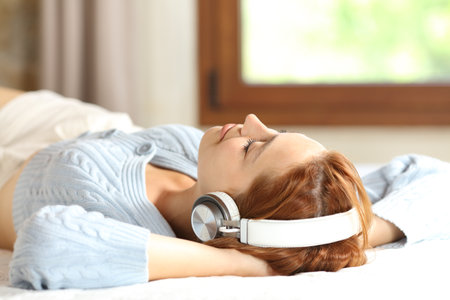 Relaxed woman resting lying on a bed listening to music with wireless headphones at homeの写真素材