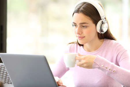 Relaxed woman using laptop and wireless headphones drinking coffee in a barの写真素材
