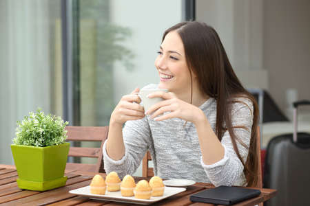 Woman having breakfast with coffee and muffins sitting on a hotel room balconyの写真素材