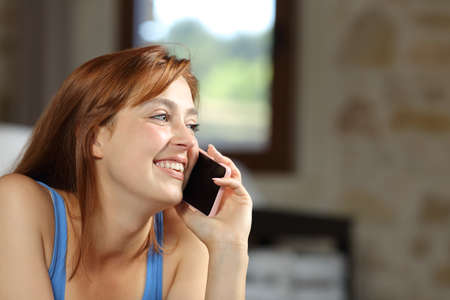 Happy woman talking on mobile phone in the bedroom at homeの写真素材