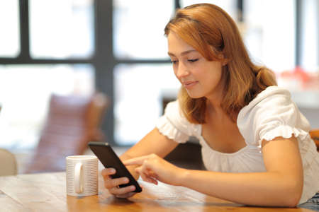 Relaxed woman using smart phone sitting in the living room at homeの写真素材