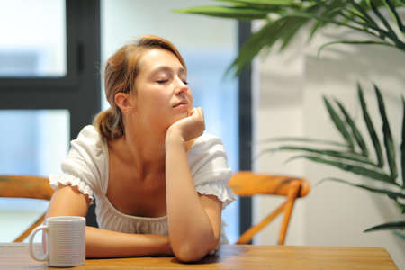 Woman resting sitting in a table at home with closed eyesの写真素材