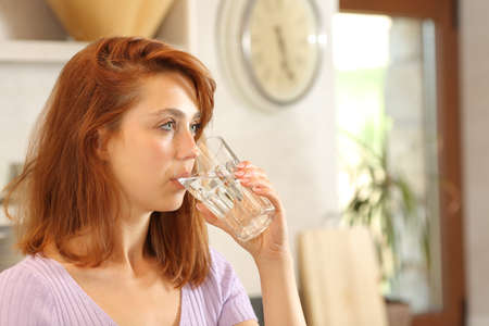 Serious woman drinking tap water looking away in the kitchenの写真素材