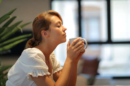 Profile of a relaxed woman smelling coffee cup sitting at homeの写真素材
