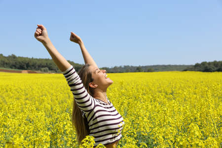 Excited woman raising arms in a yellow field celebrating spring a sunny dayの写真素材