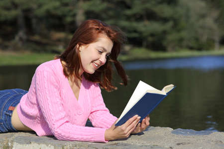 Happy woman reading a paper book lying in the mountainの写真素材
