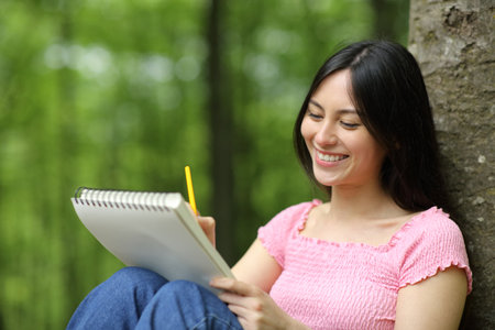 Asian happy woman drawing on notebook sitting in a forestの写真素材