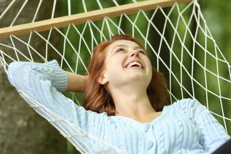 Happy woman laughing lying on rope hammock in a forestの写真素材