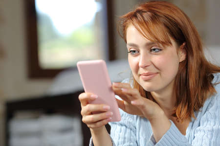 Satisfied woman checking smart phone in the bedroom at homeの写真素材