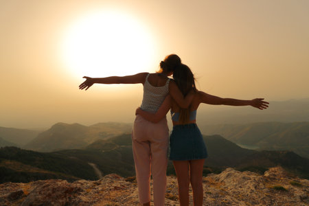 Two happy friends celebrating outstretching arms at sunset in the mountainの写真素材