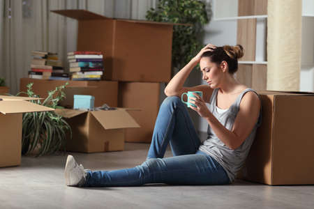 Sad evicted woman moving home complaining sitting on the floor in the nightの写真素材