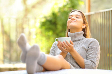 Carefree woman breathing fresh air relaxing drinking coffee in a garden at home in winterの写真素材