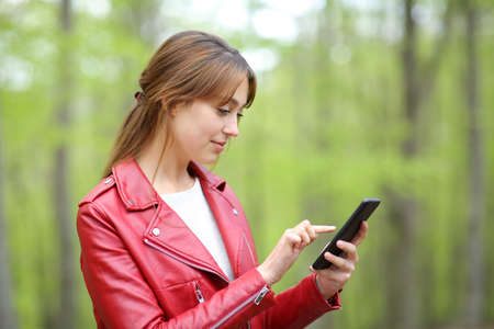 Profile of a serious woman in red checking smart phone in a forestの写真素材